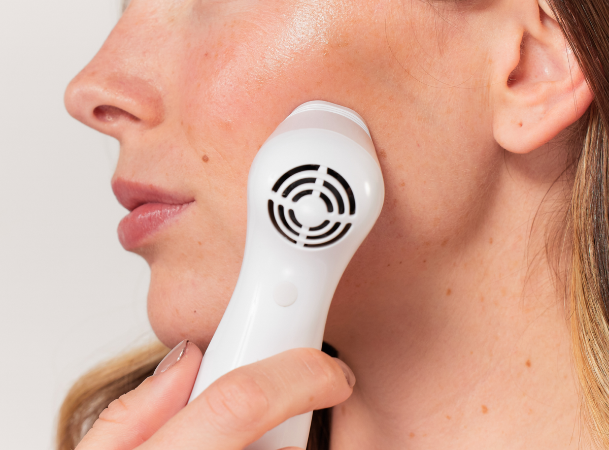 Woman using an anti-aging laser on her face after applying peptide cream 
